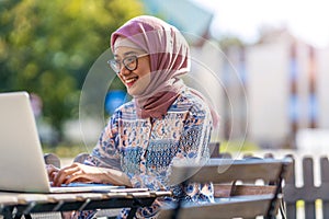 Young Muslim woman using a laptop in outdoor cafe