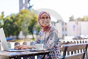 Young Muslim woman using a laptop in outdoor cafe