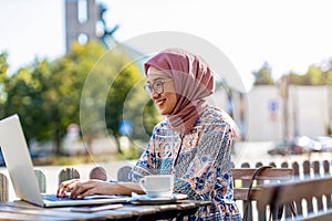 Young Muslim woman using a laptop in outdoor cafe