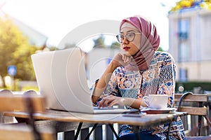 Young Muslim woman using a laptop in outdoor cafe