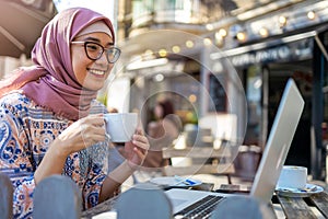 Young Muslim woman using a laptop in outdoor cafe