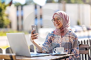 Young Muslim woman using mobile phone in outdoor cafe