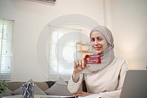 A young Muslim woman wearing a hijab sat contentedly shopping online and holding a credit card.