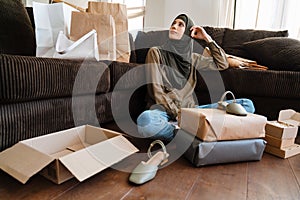 Young muslim woman wearing hijab sitting on floor with sopping bags