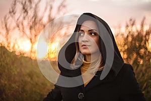 Young mysterious woman in black hood in nature at sunset photo