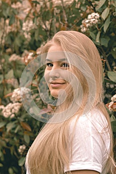 Young natural blonde woman standing in front of a flowering bush