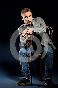 Young negligent man with cane sitting on chair