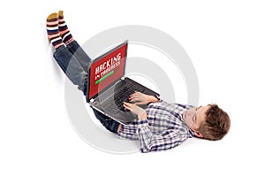 Young nerd boy lying on floor and hacking using a laptop