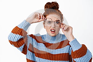 Young nerdy girl with ginger hair and blue eyes, trying to wear crooked broken glasses, cant see without eyewear