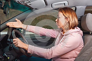 A young nervous woman is sitting behind the wheel of a right-handed car and cursing, points to the road with her hand