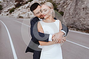 Young newly wed couple, bride and groom kissing, hugging on perfect view of mountains