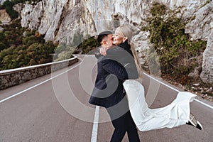 Young newly wed couple, bride and groom kissing, hugging on perfect view of mountains