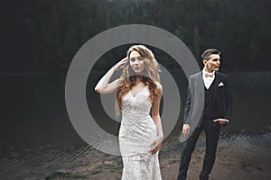 Young newly wed couple, bride and groom kissing, hugging on perfect view of mountains, blue sky