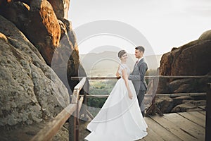 Young newly wed couple, bride and groom kissing, hugging on perfect view of mountains, blue sky