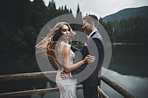 Young newly wed couple, bride and groom kissing, hugging on perfect view of mountains, blue sky