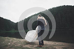 Young newly wed couple, bride and groom kissing, hugging on perfect view of mountains, blue sky