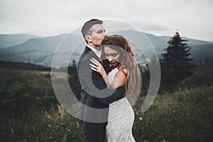 Young newly wed couple, bride and groom kissing, hugging on perfect view of mountains, blue sky