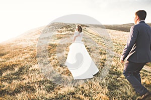 Young newly wed couple, bride and groom kissing, hugging on perfect view of mountains, blue sky