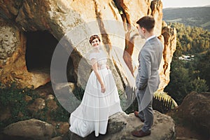 Young newly wed couple, bride and groom kissing, hugging on perfect view of mountains, blue sky