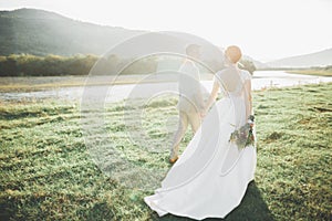 Young newly wed couple, bride and groom kissing, hugging on perfect view of mountains, blue sky