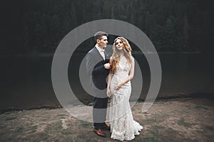 Young newly wed couple, bride and groom kissing, hugging on perfect view of mountains, blue sky