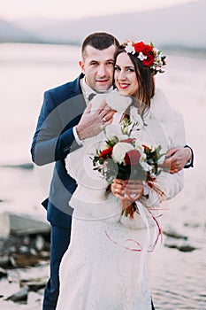 Young newlywed bridal couple posing on pebble beach near the mountain river