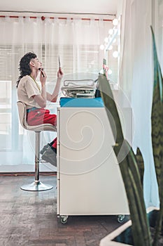 Young non-binary person applying makeup in front of a mirror in a bright room photo