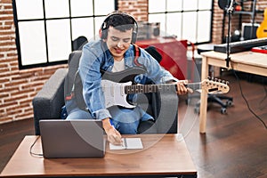 Young non binary man musician composing song playing electrical guitar at music studio