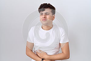 Young non binary man wearing casual white t shirt with hand on stomach because indigestion, painful illness feeling unwell