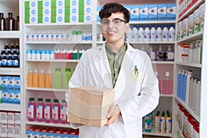 Young non binary man working at pharmacy drugstore holding box looking positive and happy standing and smiling with a confident