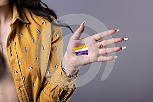 Young non-binary woman showing non-binary gender flag in hand. Close-up