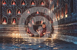 Young novice monks lighting up candlelight inside a Buddhist temple, low light setting, Shan state, Myanmar