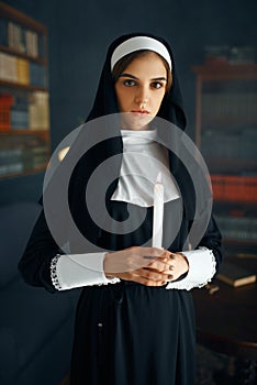 Young nun in a cassock holds a candle