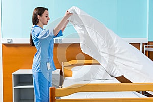 Young nurse in blue unifrom changing bedsheets of hospital bed