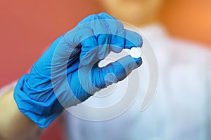 A young nurse, a doctor in blue rubber gloves, holds a white pill between her fingers. Close-up of an antibiotic in the hand for t