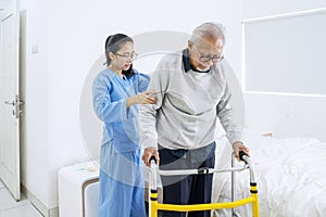Young nurse helping senior man to walk in bedroom