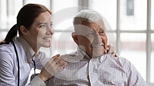 Young nurse hugs old man patient smiling look at distance