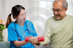 Young nurse physiotherapist support senior old man to lifting dumbell at home