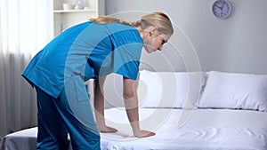 Young nurse preparing clean bed-linen in rehabilitation center, good service