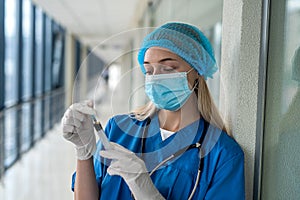 young nurse in uniform and mask holding a syringe in his hands on the corridor