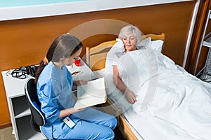 Young nurse in uniform is reading a book for her patient