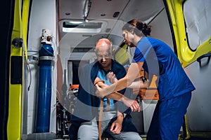 Young nurse wraps a tourniquet around a hand of her patient in an ambulance car