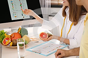 Young nutritionist consulting patient at table in clinic