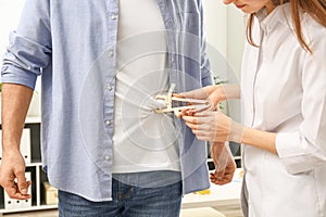 Young nutritionist measuring patient`s body fat with caliper in clinic