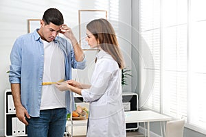 Young nutritionist measuring patient`s waist