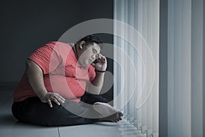 Young obese man looks stressed near the window