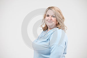 Young obese woman in casual blue clothes on a white background in the studio. Bodypositive.