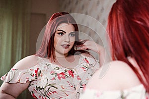 Young obese woman in casual flower clothes looking in the mirror. Bodypositive and improper nutrition. back view