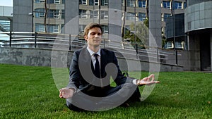 Young office manager sitting in lotus position, meditating on grass, freedom