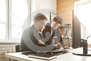 Young office worker sitting at desk, using computer. Two business man talking